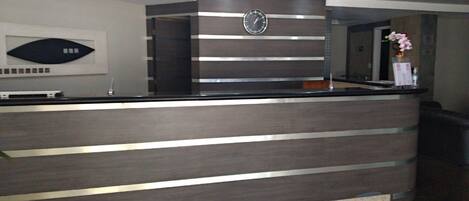 A reception desk with a clock above it, a flower vase, and a modern design with horizontal lines.