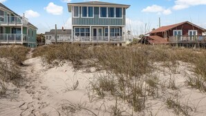 Une propriété située en bord de mer, avec une maison à deux étages dotée de grandes fenêtres et d’un balcon.