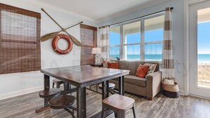 Un salon avec une table en bois, un canapé et une grande fenêtre donnant sur la plage.