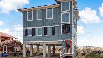 A two-story building with a balcony, a red door, and a sandy ground.