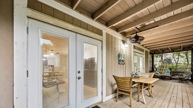 A covered patio with a wooden table and chairs, a door with glass panels, and a hanging light fixture. - Amelia Landings Condo, Easy Access to the Pool and Short Walk to the Beach by RedAwning (Fernandina Beach)