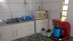 A kitchen with white cabinets, a granite countertop, a microwave, a red coffee maker, and a sink. - Pousada Recanto do Luar (Taubate)