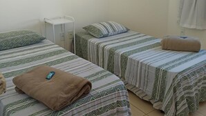 A room with two beds, a small white table, a framed picture on the wall, and a curtain on the window. - Pousada Recanto do Luar (Taubate)