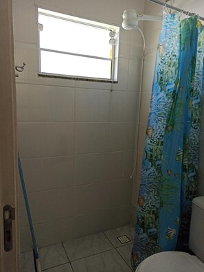 A small bathroom with a window, a shower curtain with fish patterns, and a toilet.