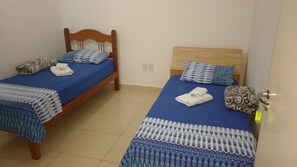 Two single beds with wooden frames and blue bedding, a patterned pillow, and a towel on each bed.