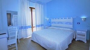 A bedroom with a bed, a chair, a nightstand, and a window with curtains. - Bed & Breakfast Selvaggio Blu (Baunei)