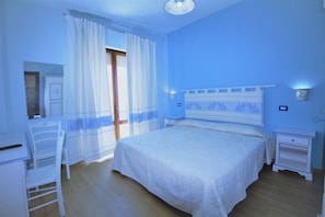 A bedroom with a bed, a chair, a nightstand, and a window with curtains. - Bed & Breakfast Selvaggio Blu (Baunei)