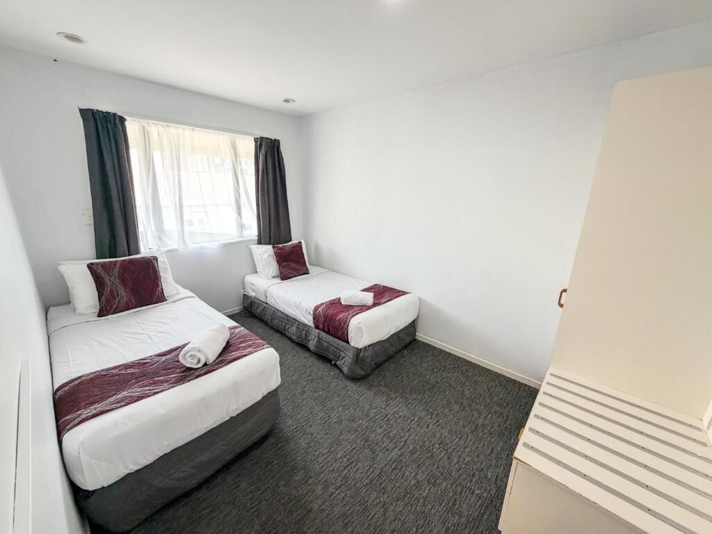 A hotel room with two beds, a window with curtains, and a carpeted floor.
