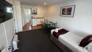 Habitación de hotel compacta con una cama individual, un escritorio pequeño y una kitchenette al fondo.