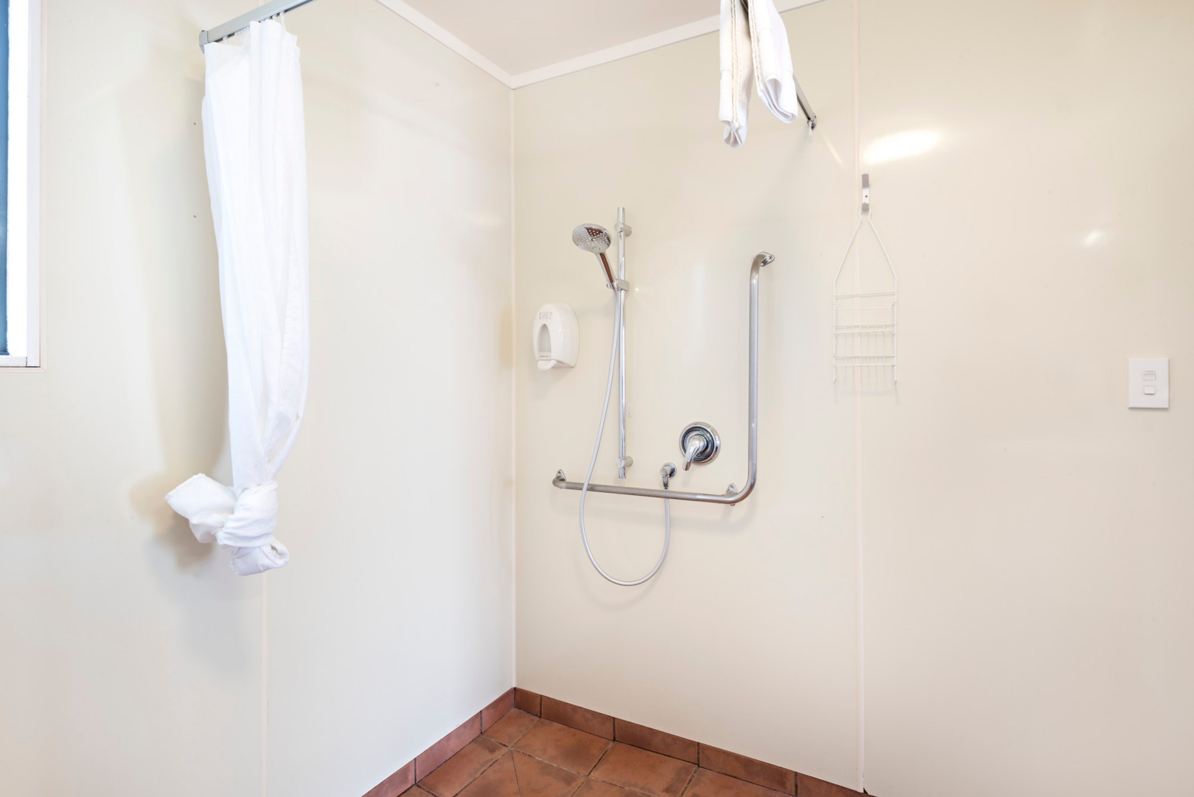 A bathroom with a shower, a towel rack, and a hand dryer.