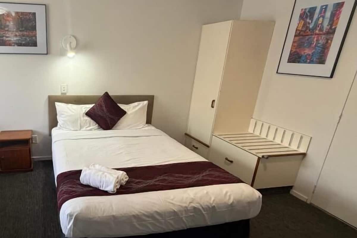 Une chambre d’hôtel comprenant un lit, une armoire, une table de chevet et un luminaire fixé au mur.