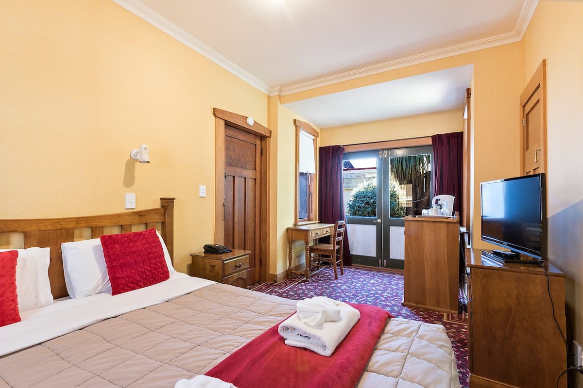 Une chambre d’hôtel avec un lit, un bureau, une chaise, une télévision et une fenêtre avec des rideaux.