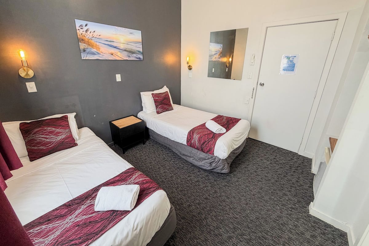 Une chambre d’hôtel avec deux lits, une petite table de chevet, un miroir fixé au mur et un tableau représentant un coucher de soleil.