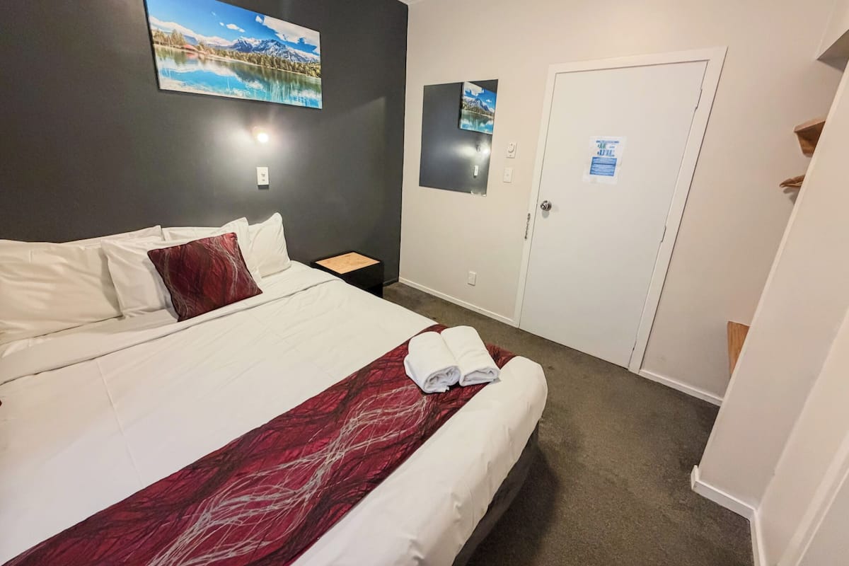 Une chambre d’hôtel avec un grand lit, une table de chevet, une porte et deux tableaux accrochés au mur.