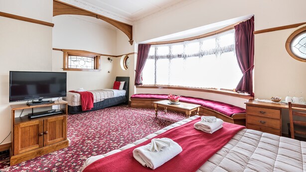 Un dormitorio con una cama grande, televisión, armario de madera, ventana con cortinas y alfombra roja.