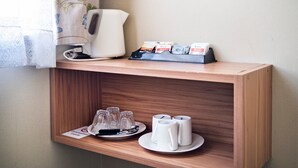 Zona de recepción de hotel con una máquina de café, bolsitas de té y una bandeja de vasos y tazas.