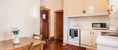 A kitchen with a wooden table, chairs, a microwave, a stove, and an exit sign.