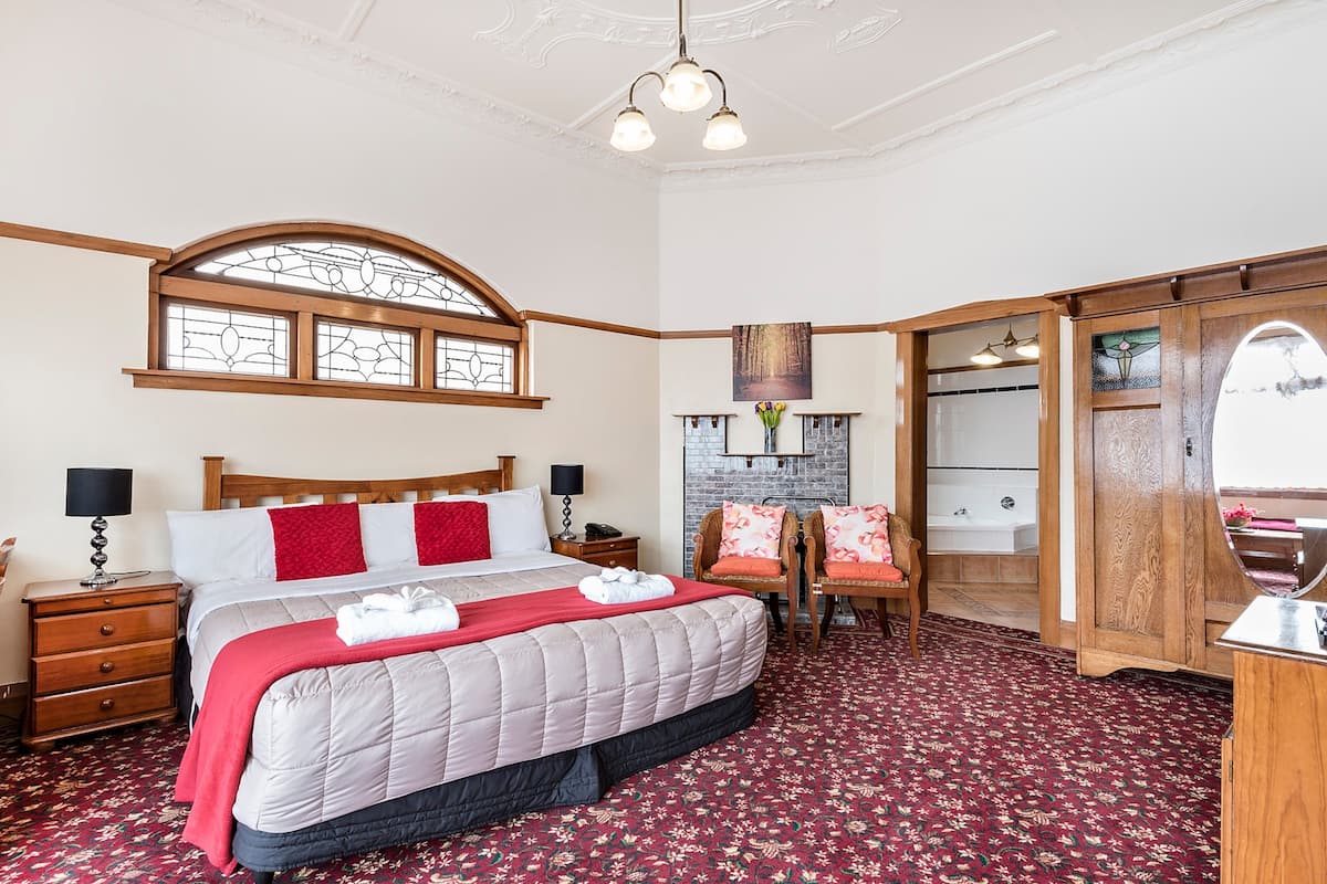 Une chambre à coucher avec un grand lit, une tête de lit en bois, une fenêtre avec des vitraux, une cheminée en pierre et une armoire en bois.