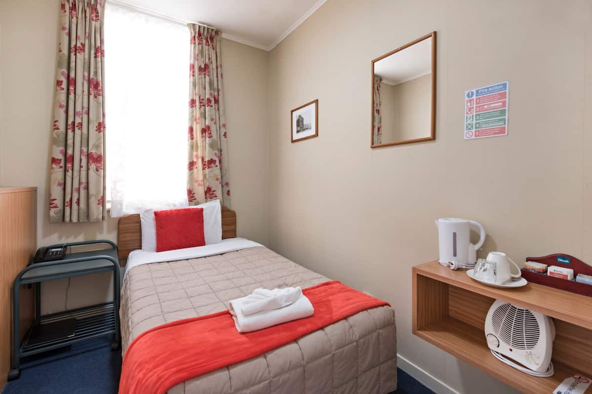 Une chambre d’hôtel avec un lit, une table de chevet avec une bouilloire, un ventilateur et un miroir au mur.