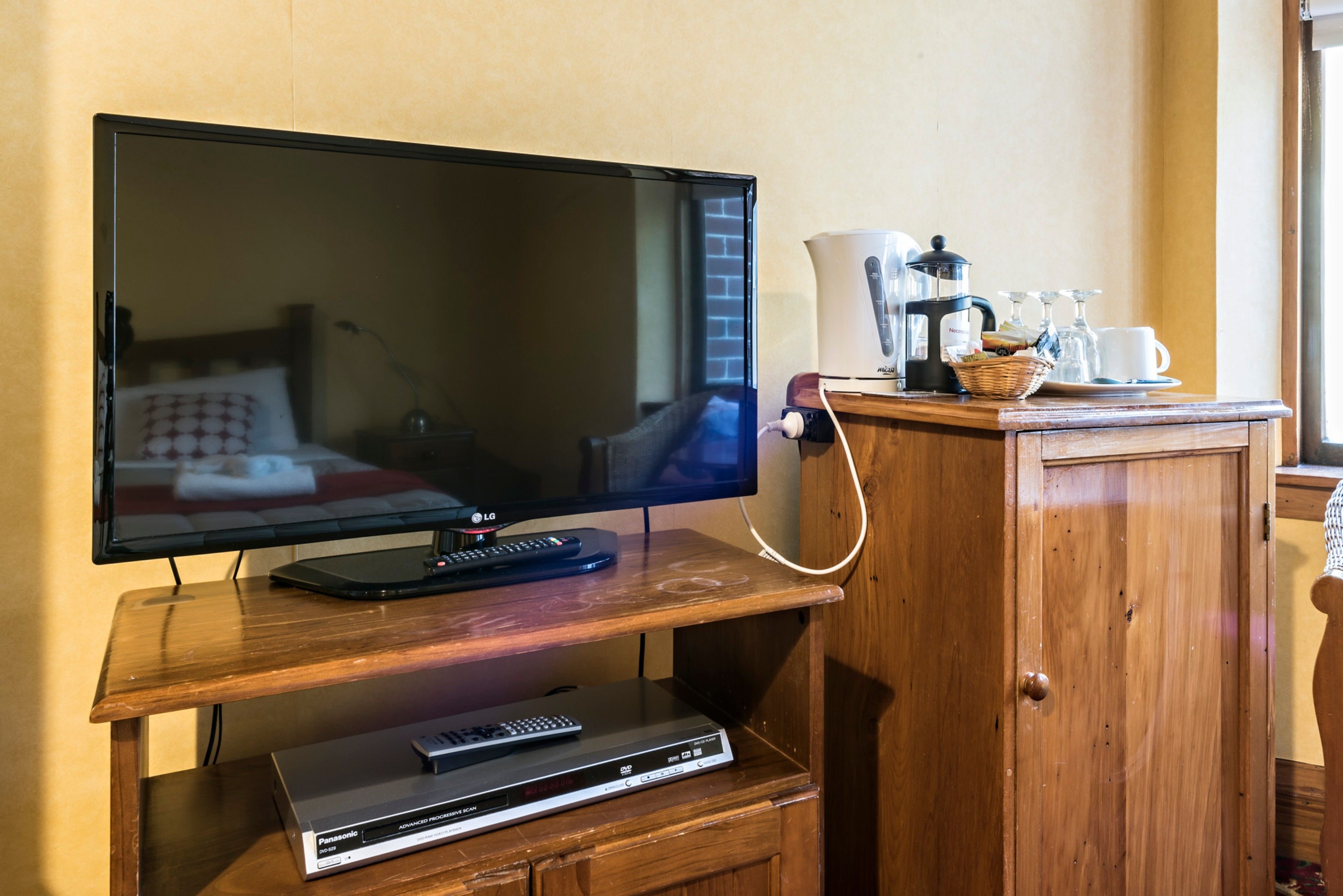 A television on a wooden stand with a remote control, a DVD player, and a coffee maker on a wooden cabinet.