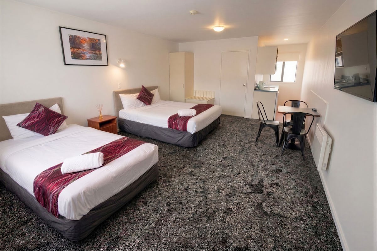 Une chambre d’hôtel avec deux lits, un bureau, une chaise, une petite table, un miroir et un tableau au mur.