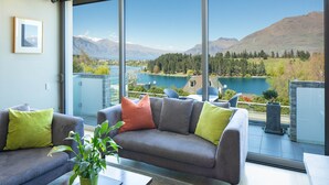 A modern living room with a large window overlooking a lake and mountains. - Hello QT Pounamu (Queenstown)