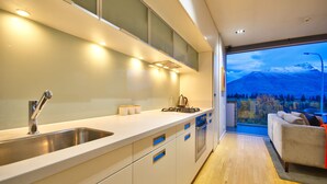 A modern kitchen with a stainless steel sink, white cabinets, and a view of a snowy mountain through a large window. - Hello QT Pounamu (Queenstown)