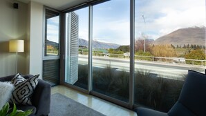 A modern room with large windows, a sofa, and a lamp. - Hello QT Pounamu (Queenstown)