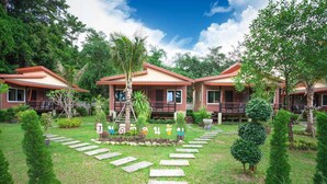 A row of three brick houses with red roofs, surrounded by lush greenery and a stone pathway leading to the entrance. - Siray Green Resort (Ratsada)