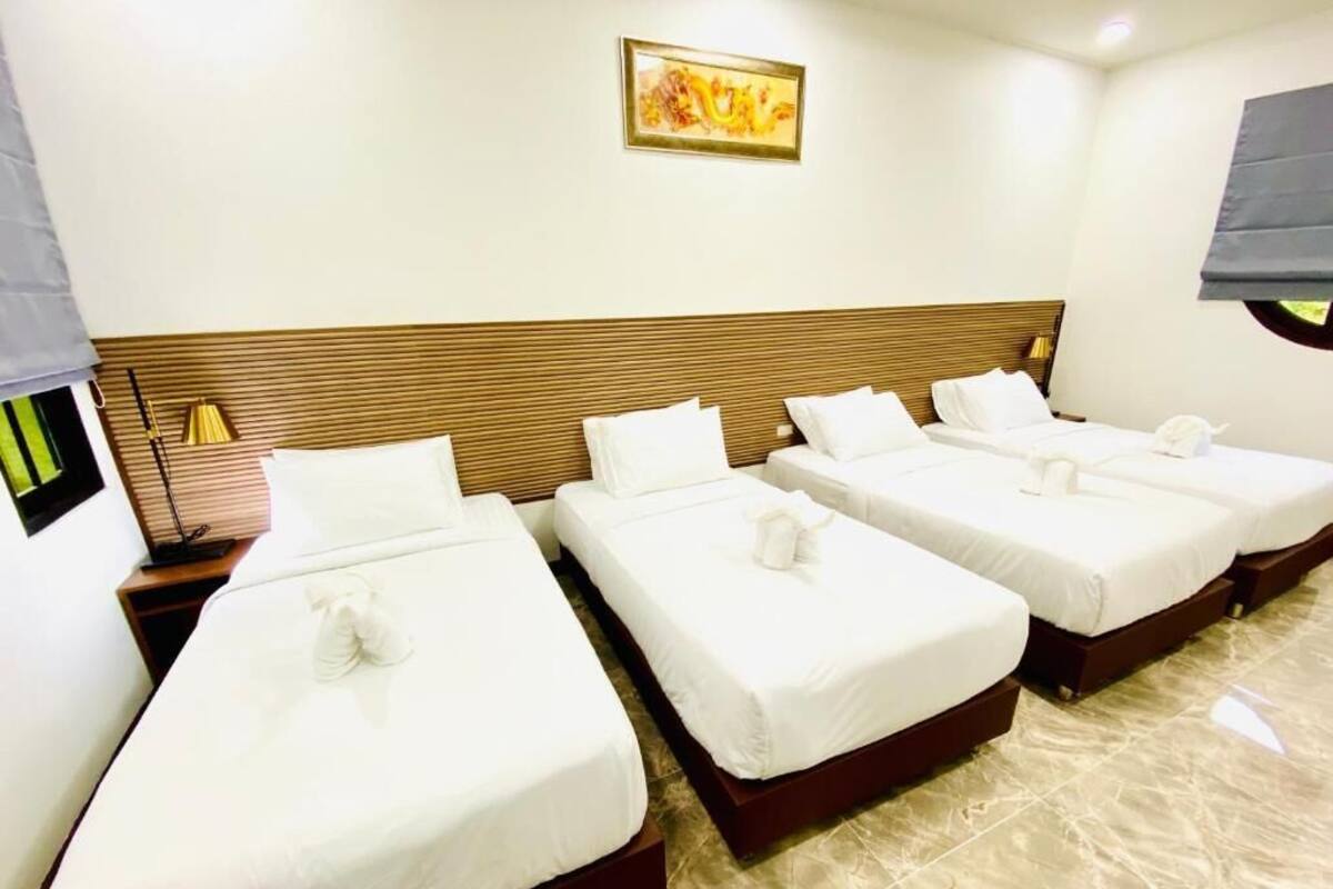 A hotel room with three beds, a wooden headboard, a painting on the wall, and a window with a blind.