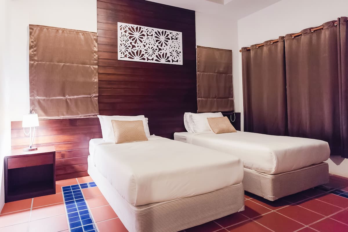 A hotel room with two beds, a nightstand, a decorative wall panel, and brown curtains.