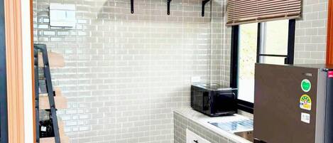 Cocina compacta con refrigerador, microondas y ventana con persianas.