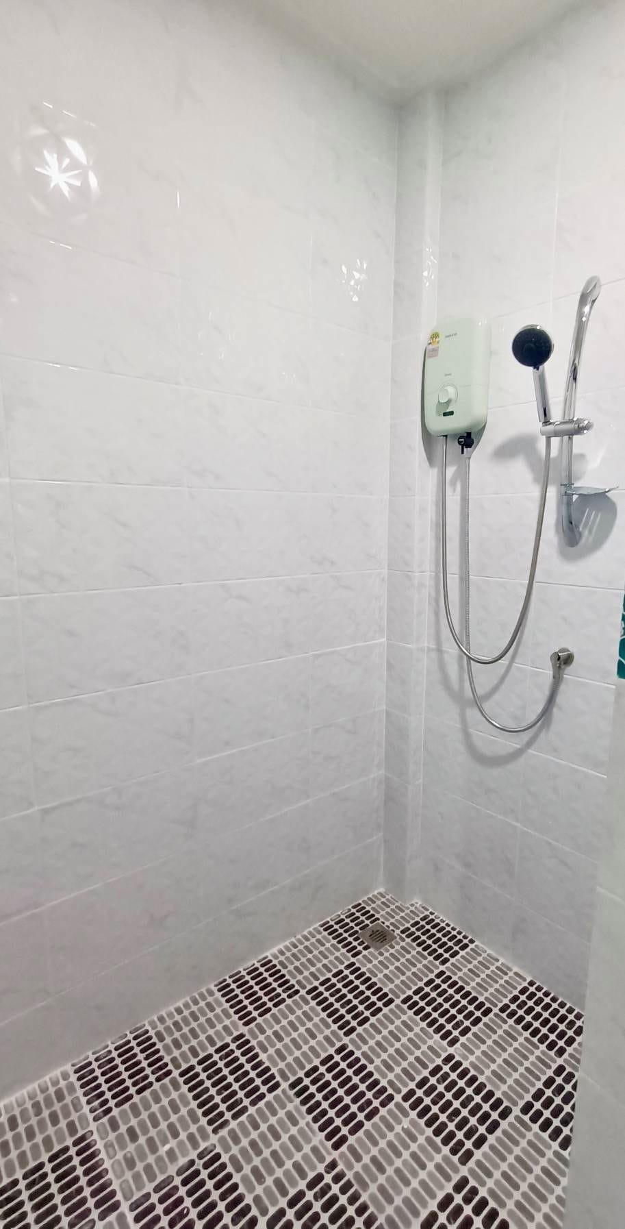 A shower area with a tiled floor, a handheld showerhead, and a wall-mounted faucet.