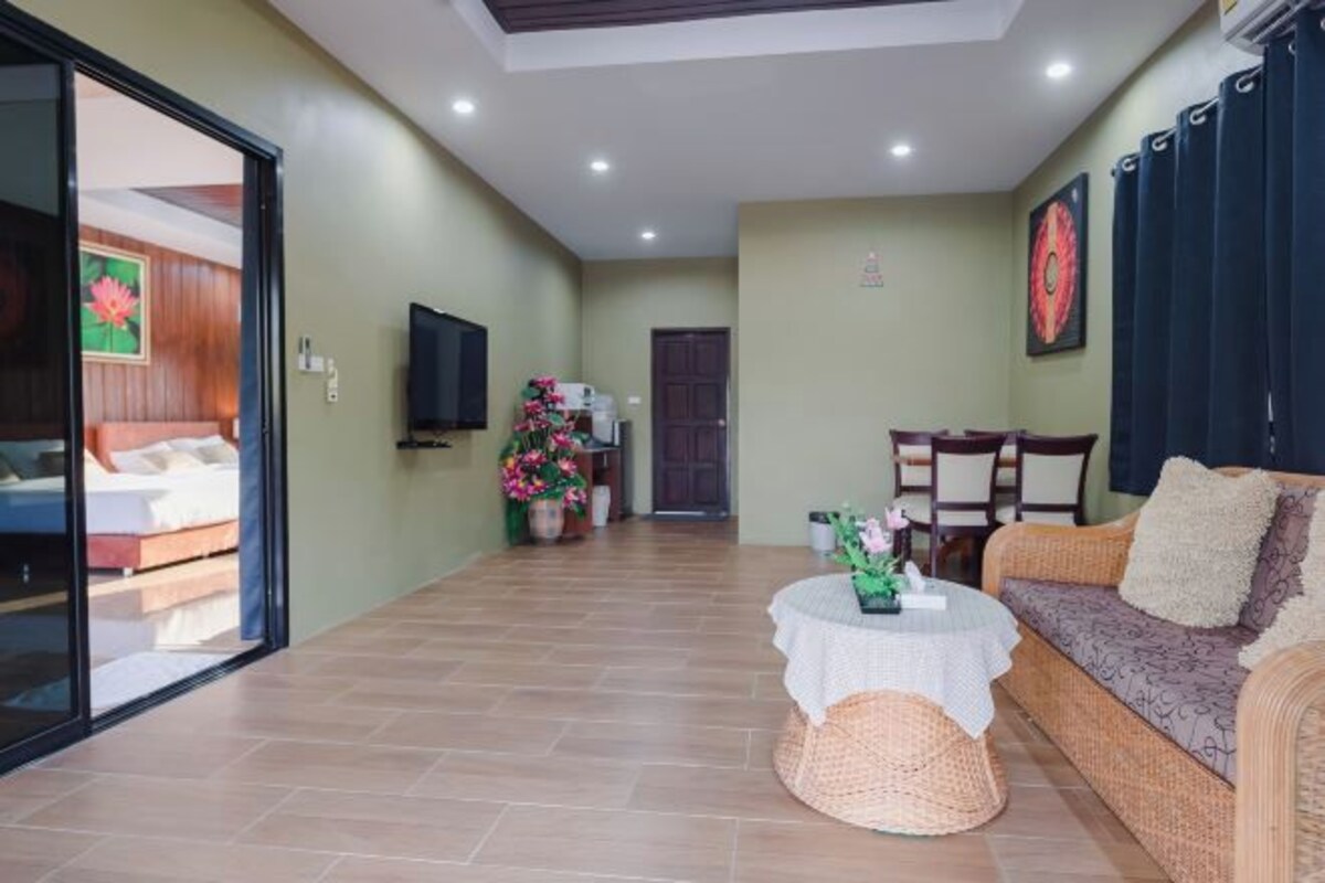 Una sala de estar con un sofá, una mesita redonda, un televisor y una puerta que da a otra habitación.