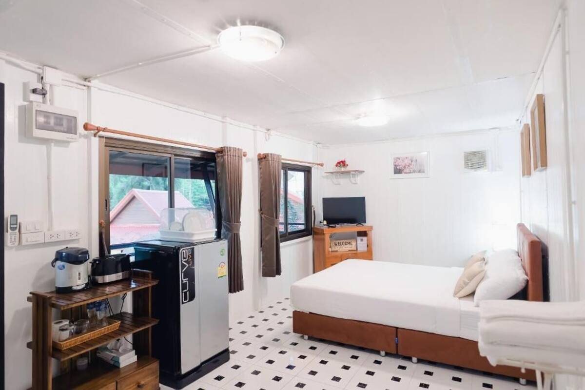 A compact hotel room with a bed, a TV, a small kitchenette, and a window.