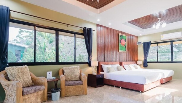 A hotel room with a bed, two chairs, a nightstand, a window with curtains, and a painting on the wall. - Siray Green Resort (Ratsada)
