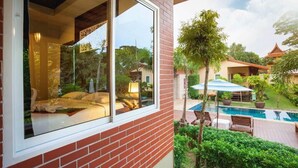 A hotel room with a large window, a view of a swimming pool, and a patio area with outdoor seating. - Siray Green Resort (Ratsada)