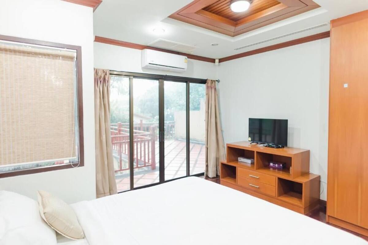 A hotel room with a bed, a TV, a wardrobe, and a sliding glass door to a balcony.