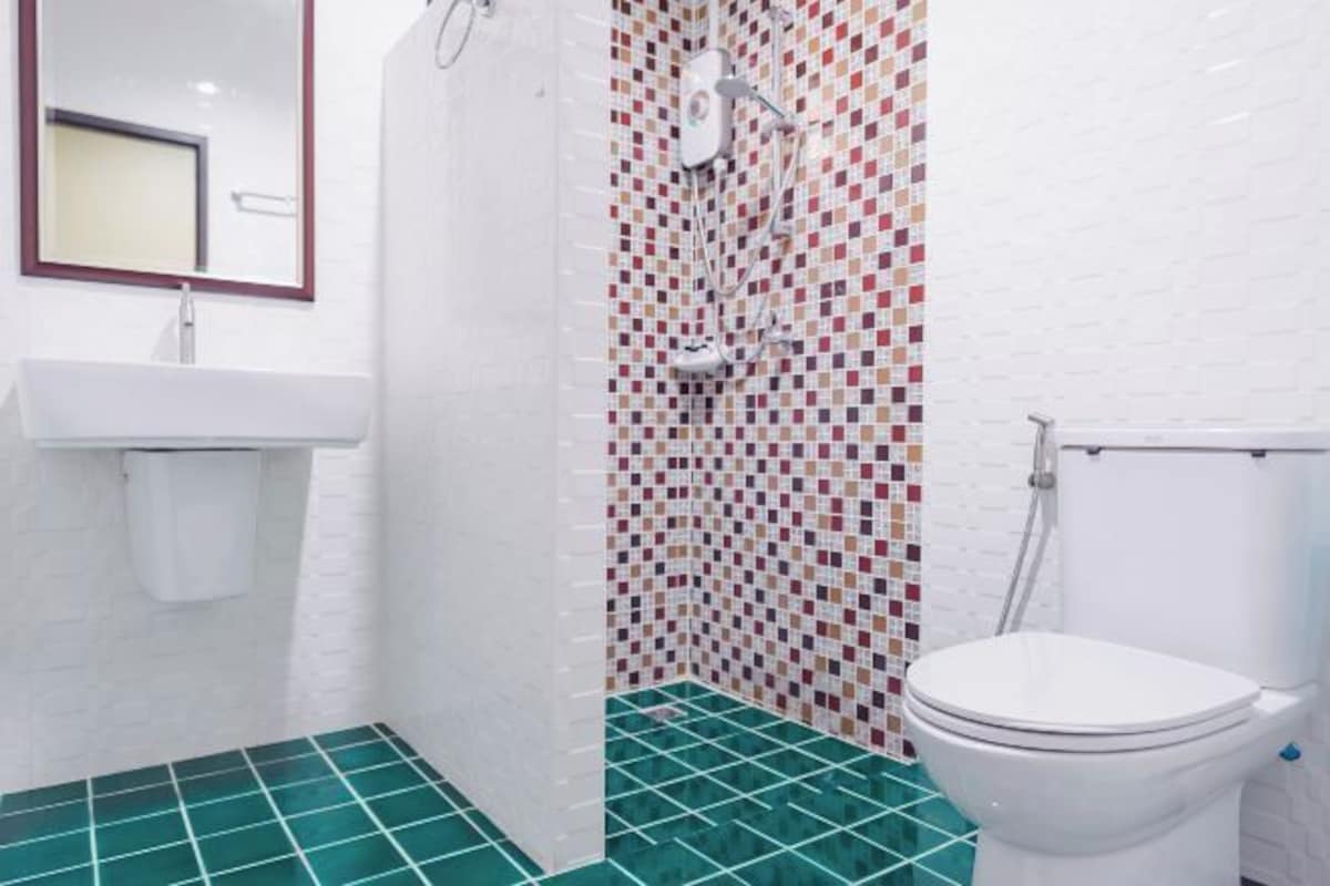 Un baño con un lavamanos blanco, un inodoro y una zona de ducha con pared de mosaicos.