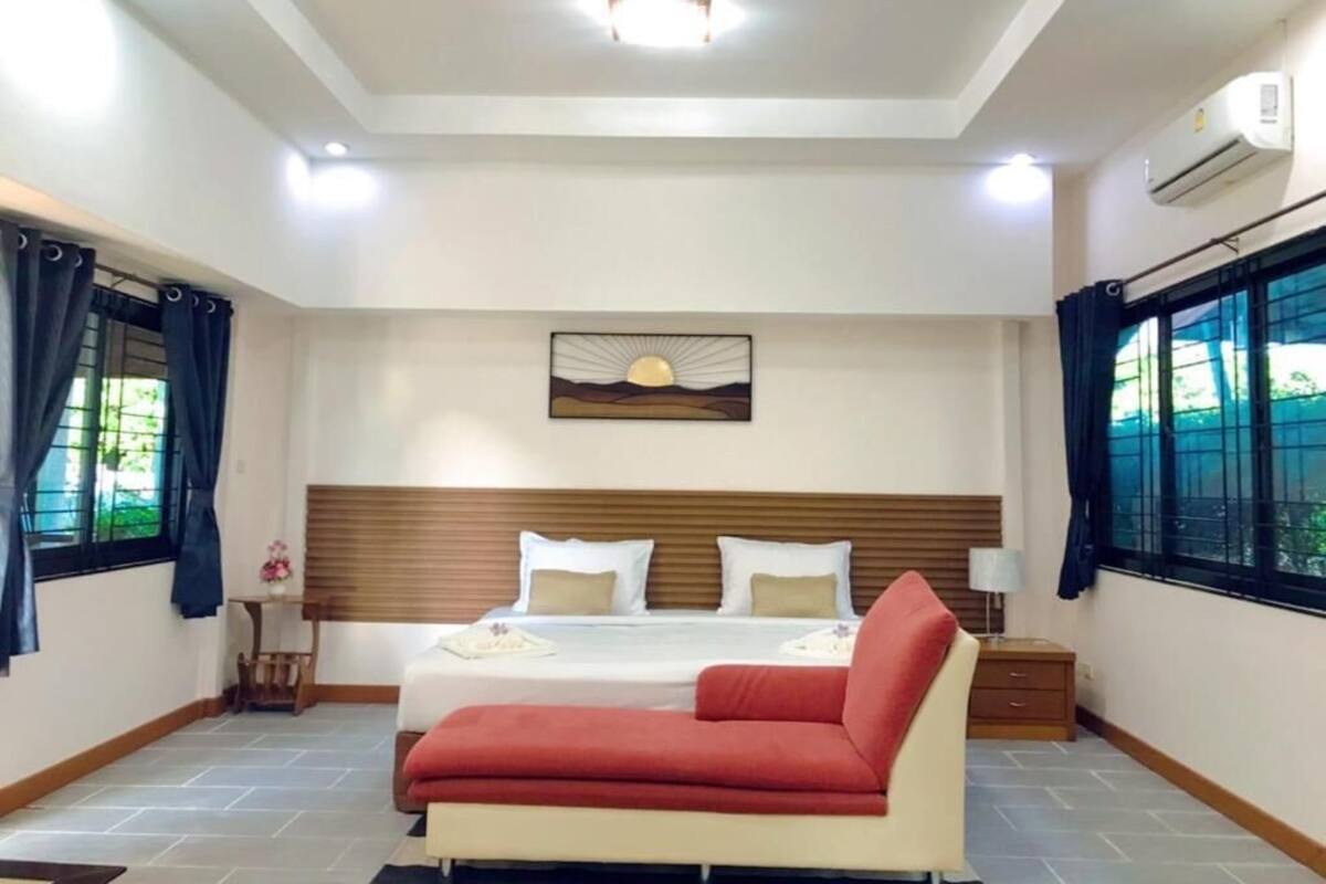 A bedroom with a bed, a red sofa, a nightstand, and a wall-mounted air conditioner.