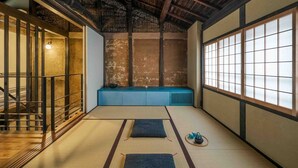 Una habitación tradicional japonesa con tatami, techo de madera, suelo de tatami, un banco bajo azul y una puerta corredera.