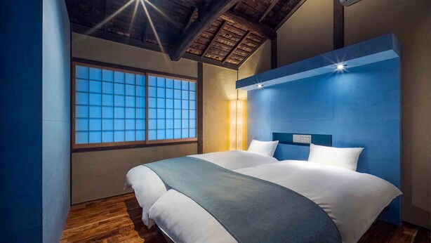 Un dormitorio con una cama grande, suelo de madera, una ventana con cristal azulado y una pared de acento azul.