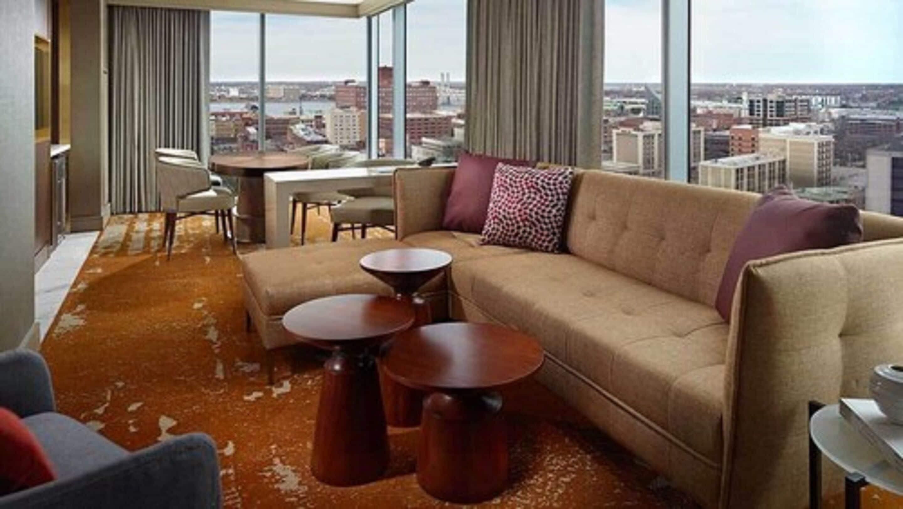 Un salon moderne doté d’une grande fenêtre, d’un canapé, de deux tables d’appoint et offrant une vue sur la ville.