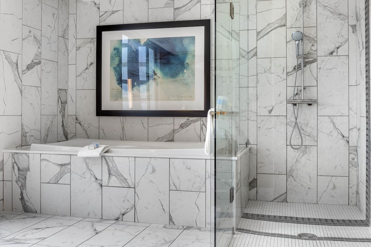A modern bathroom with a marble tile design, a framed artwork above the sink, and a glass-enclosed shower area.