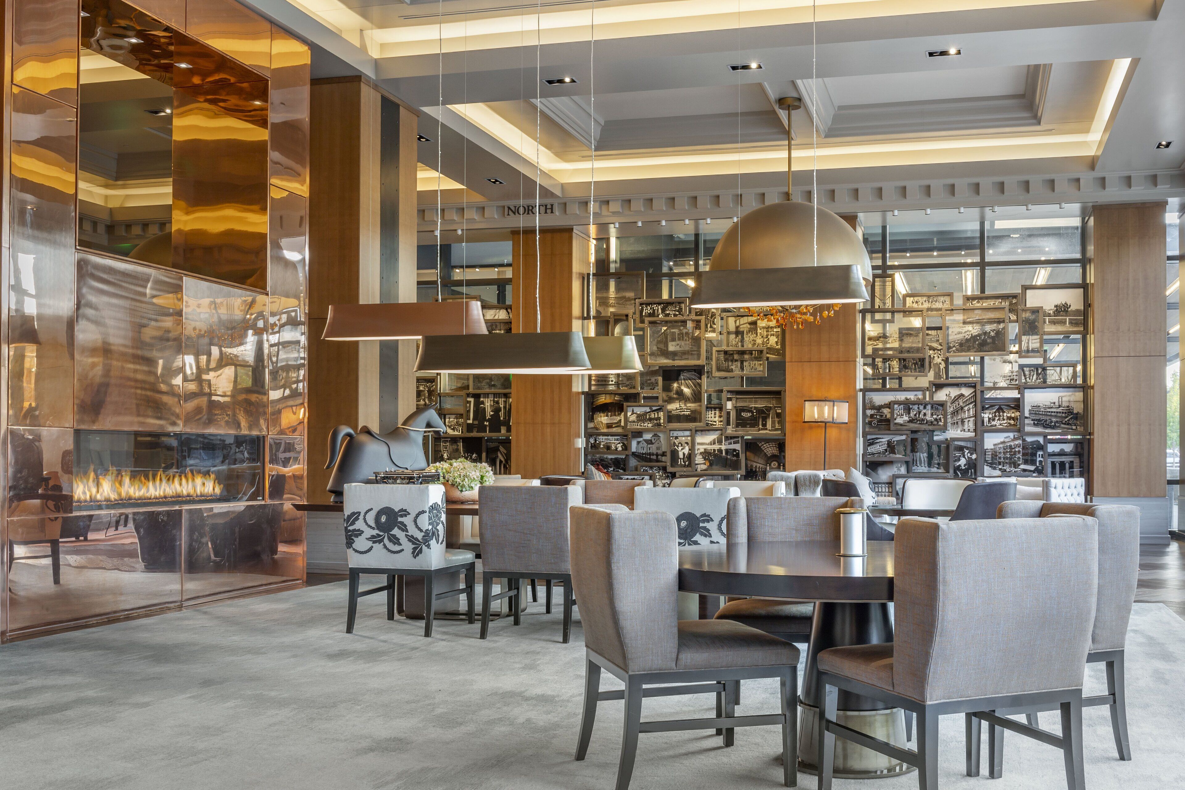 A modern hotel lobby with a fireplace, seating area, and a display of framed pictures.