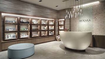 A modern reception area with a large, round, white reception desk, wooden shelving with various products, and a textured wall with the name 'MOKARA'.