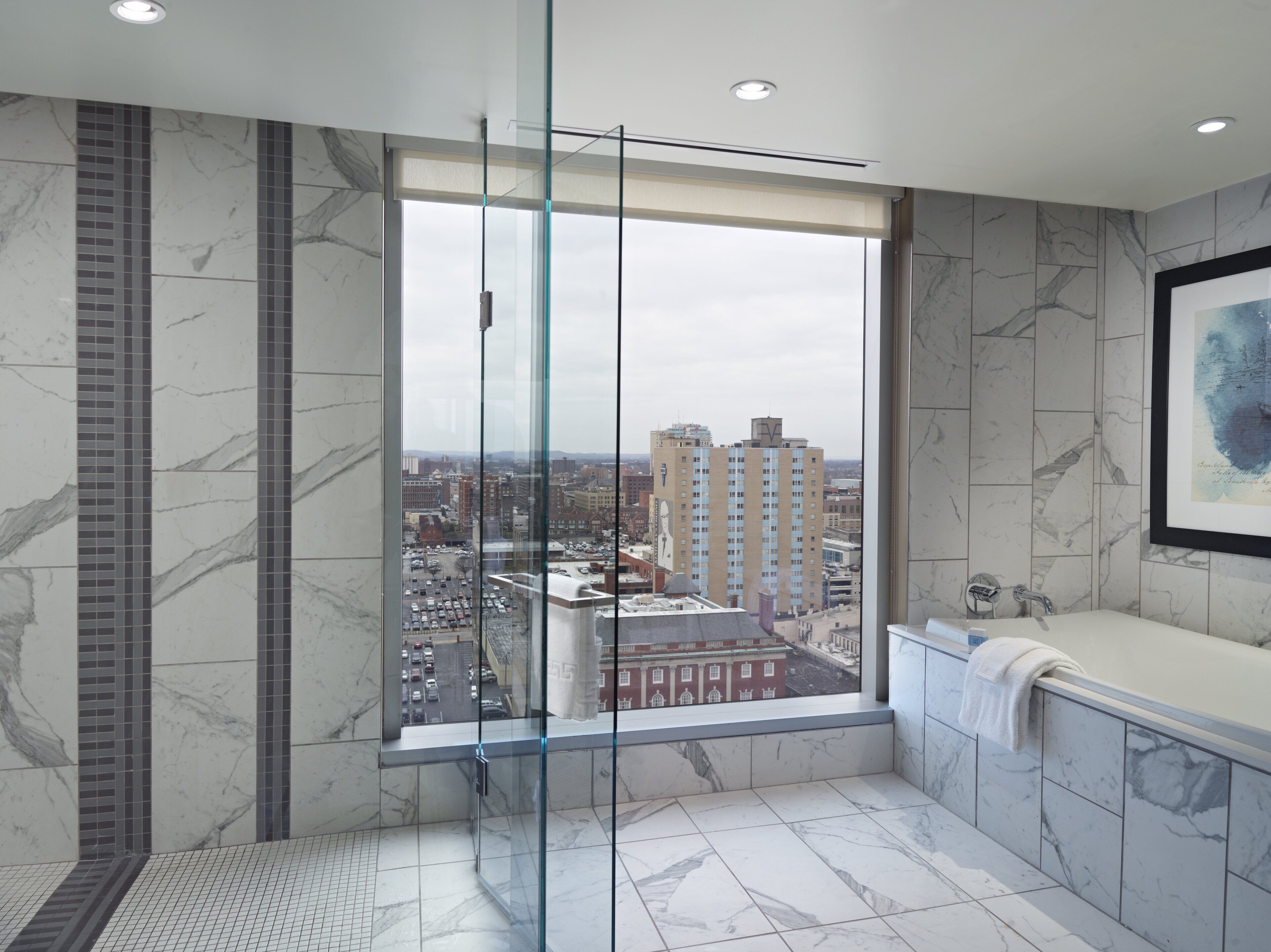 A modern bathroom with a large window, marble walls, and a bathtub.