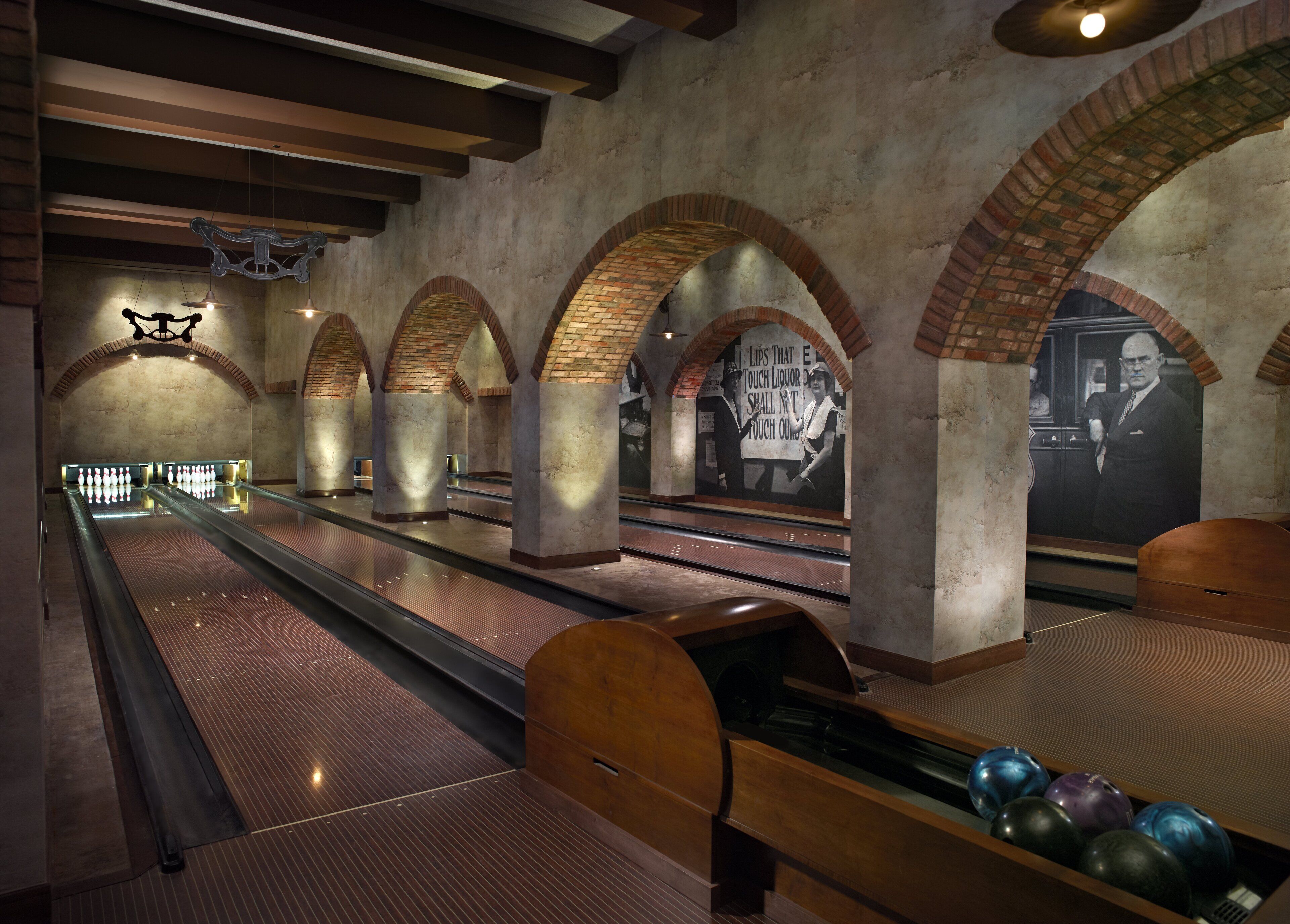 A bowling alley with multiple lanes, wooden bowling pins, and a mural on the wall.