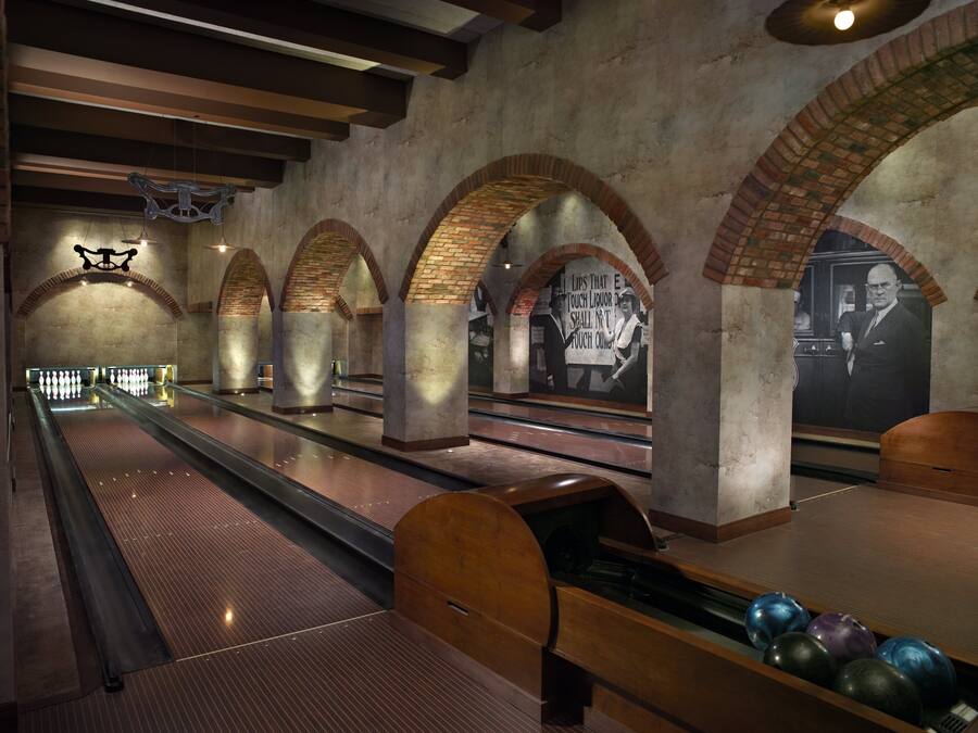 En bowlinghal med flere baner, træbowlingkegler og et muralmaleri på væggen.