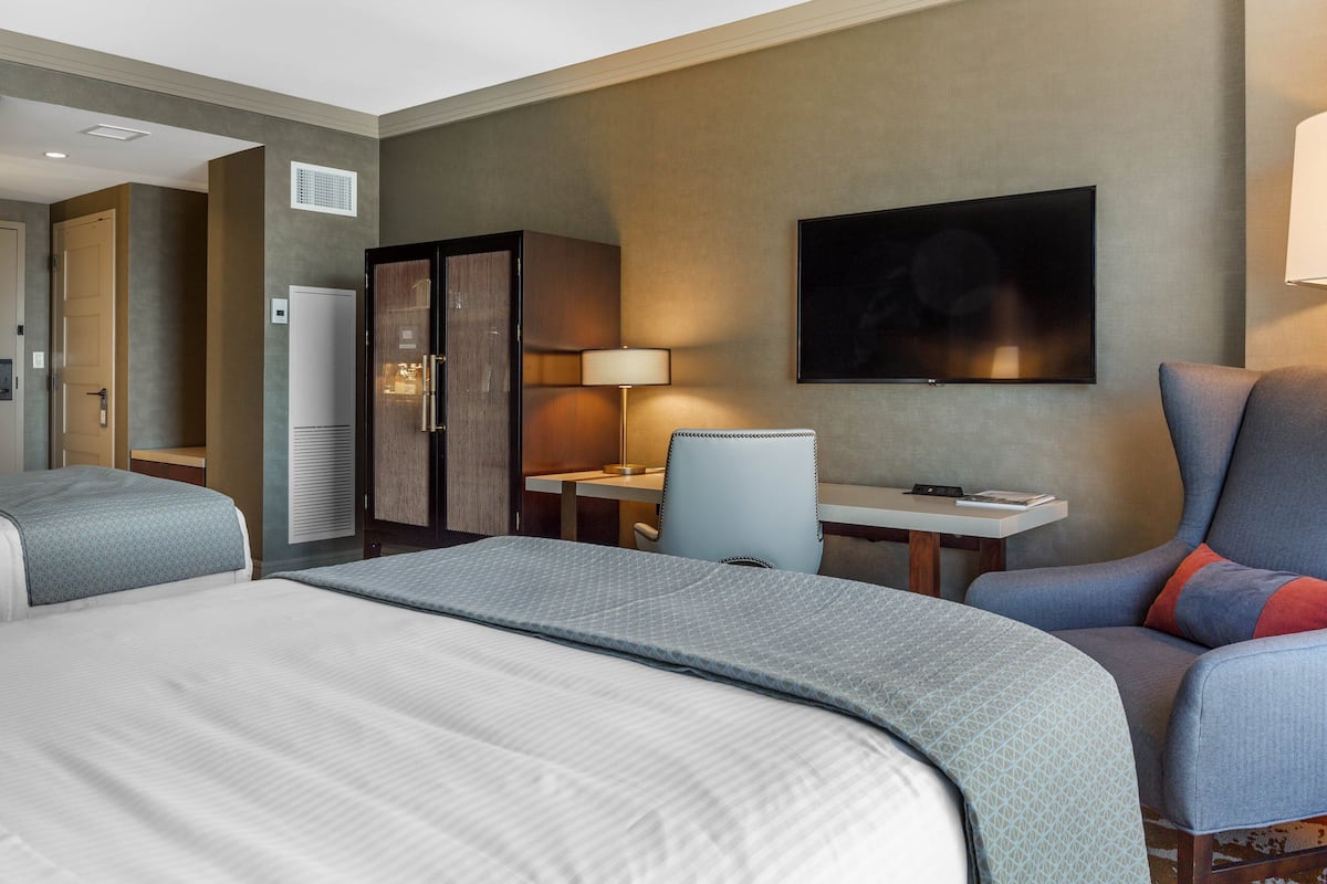 A hotel room with two beds, a desk, a chair, a TV, and a wardrobe.